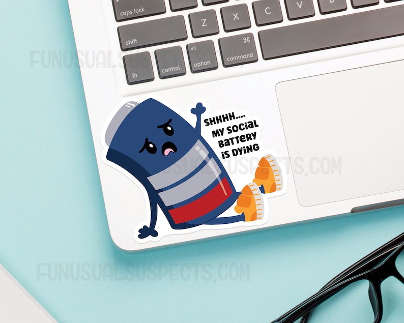 K&ouml;nnte beinhalten: Ein blauer und roter Batterie-Charakter mit einem traurigen Gesicht und dem Text "SHHHH.... MY SOCIAL BATTERY IS DYING" auf einem wei&szlig;en Laptop.
