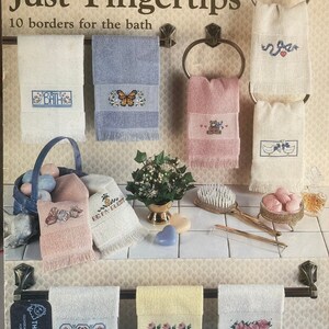 Puede incluir: Un folleto titulado "Just Fingertips" con 10 bordes para el ba&ntilde;o. El folleto presenta im&aacute;genes de toallas con dise&ntilde;os bordados, incluyendo una mariposa, un osito de peluche y un par de patos. El folleto es de Leisure Arts.