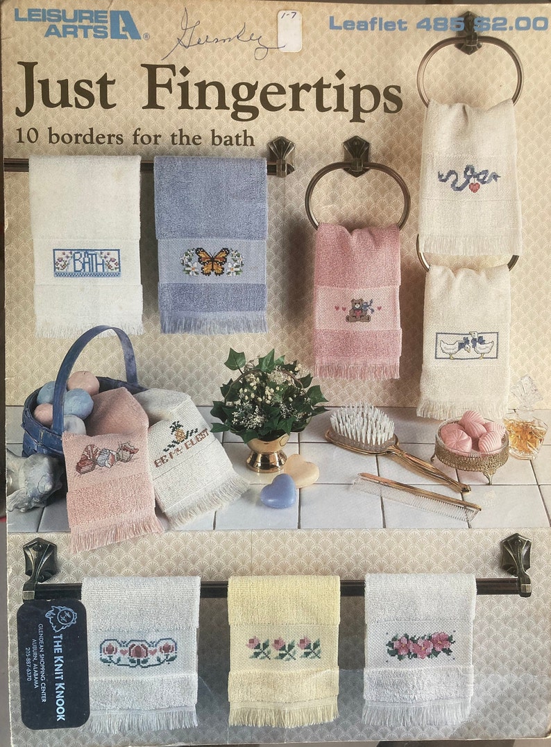 Puede incluir: Un folleto titulado "Just Fingertips" con 10 bordes para el ba&ntilde;o. El folleto presenta im&aacute;genes de toallas con dise&ntilde;os bordados, incluyendo una mariposa, un osito de peluche y un par de patos. El folleto es de Leisure Arts.