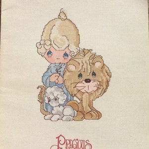 May include: Cross stitch pattern featuring a Precious Moments character, a blonde-haired boy with blue eyes, holding a flower and standing with a lion and a lamb. The pattern is titled "Peace on Earth" and is from book PM-4.