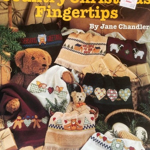 Puede incluir: Una colecci&oacute;n de patrones de punto de cruz para toallas de dedos de Navidad de estilo r&uacute;stico. Los patrones presentan una variedad de dise&ntilde;os, incluyendo un oso de peluche, un hombre de jengibre, un &aacute;rbol de Navidad y una corona. Los patrones est&aacute;n impresos sobre un fondo marr&oacute;n con texto blanco. El texto de la portada dice "Country Christmas Fingertips" y "By Jane Chandler".
