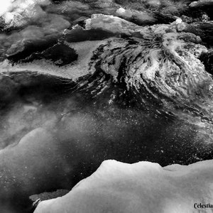 Op de afbeelding: Zwart-witte abstracte foto van een draaiend patroon van ijs en water. De afbeelding heeft een donkere, sombere sfeer en roept een gevoel van winter en kou op.