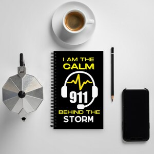 Puede incluir: Una libreta negra de espiral con un gráfico amarillo y blanco de un auricular 911 y el texto "I am the calm 911 behind the storm".