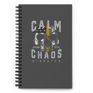 Puede incluir: Una libreta espiral gris con un gráfico desgastado de una calavera con una bandera estadounidense y una franja amarilla. El texto "Calm Among Total Chaos Dispatch" está impreso debajo de la calavera.