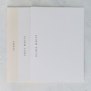 May include: Three paper samples in ivory, soft white, and ultra white. The paper is smooth and has a subtle texture.  PAPER OPTIONS is written at the top of the image.