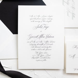 May include: A white wedding invitation with black calligraphy text. The invitation announces the marriage of Julia Faye to Garrett Allen Watson on Saturday, November 12, 2023, at 3:00 PM at Old Lystra Ann, 1164 Old Lystra Road, Chapel Hill, North Carolina. A reception will follow.