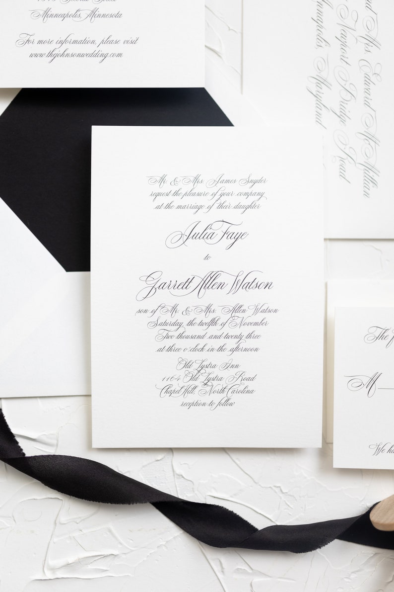 May include: A white wedding invitation with black calligraphy text. The invitation announces the marriage of Julia Faye to Garrett Allen Watson on Saturday, November 12, 2023, at 3:00 PM at Old Lystra Ann, 1164 Old Lystra Road, Chapel Hill, North Carolina. A reception will follow.