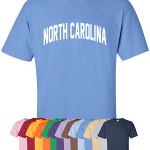 May include: A light blue t-shirt with the text "NORTH CAROLINA" in white. The shirt is available in a variety of colors, including pink, red, orange, green, purple, brown, light blue, beige, gray, and navy.