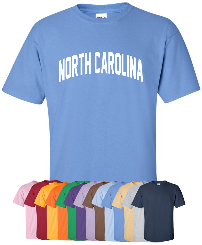 May include: A light blue t-shirt with the text "NORTH CAROLINA" in white. The shirt is available in a variety of colors, including pink, red, orange, green, purple, brown, light blue, beige, gray, and navy.