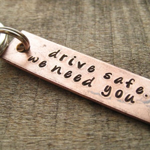 May include: Copper keychain with a silver ring. The keychain has the words "drive safe. we need you." engraved on it with a small heart symbol.