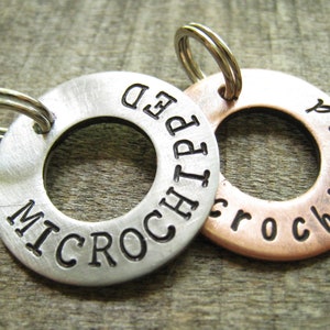 May include: Two round metal pet ID tags with a key ring. The silver tag says "MICROCHIPPED" and the copper tag says "MICROCHIPPED".