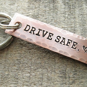 May include: A copper keychain with a hammered finish and a silver key ring. The keychain has the text "DRIVE SAFE. ♥ A" engraved on it.