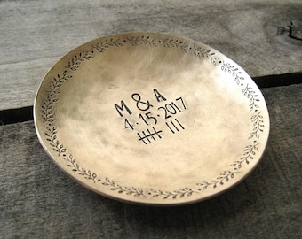 May include: A round, silver-colored dish with a decorative border of leaves. The dish is engraved with the initials "M&A" and the date "4.15.2017".