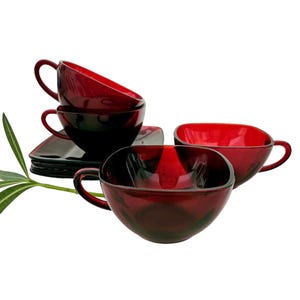 May include: Set of six ruby red glass teacups and saucers. The cups are square shaped and the saucers are round. The cups and saucers are stacked on top of each other.