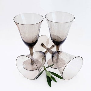 May include: Four clear glass wine glasses with a textured, bubbled surface. The glasses are arranged in a pyramid shape with the top glass upside down. A sprig of green leaves is in the center of the glasses.