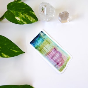 May include: A colorful abstract sticker with shades of blue, green, yellow, and purple. The sticker has a slightly irregular shape and a white border.