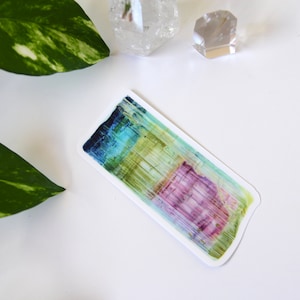 May include: A colorful abstract sticker with vertical lines in shades of blue, green, yellow, pink, and purple. The sticker has a white border and is on a white background.
