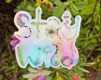Könnte beinhalten: Ein holografischer Aufkleber mit den Worten "Stay Wild" in einer verspielten Schrift. Der Aufkleber zeigt verschiedene botanische Illustrationen, darunter Pilze, Farne und Blumen.
