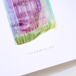 May include: A watercolor painting of a tourmaline crystal with green, purple, and blue hues. The word "TOURMALINE" is written in gray text below the crystal.