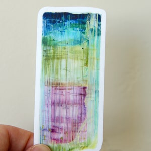 May include: A sticker featuring a colorful abstract design with shades of blue, green, pink, and white. The design resembles a crystal or gemstone with vertical lines.