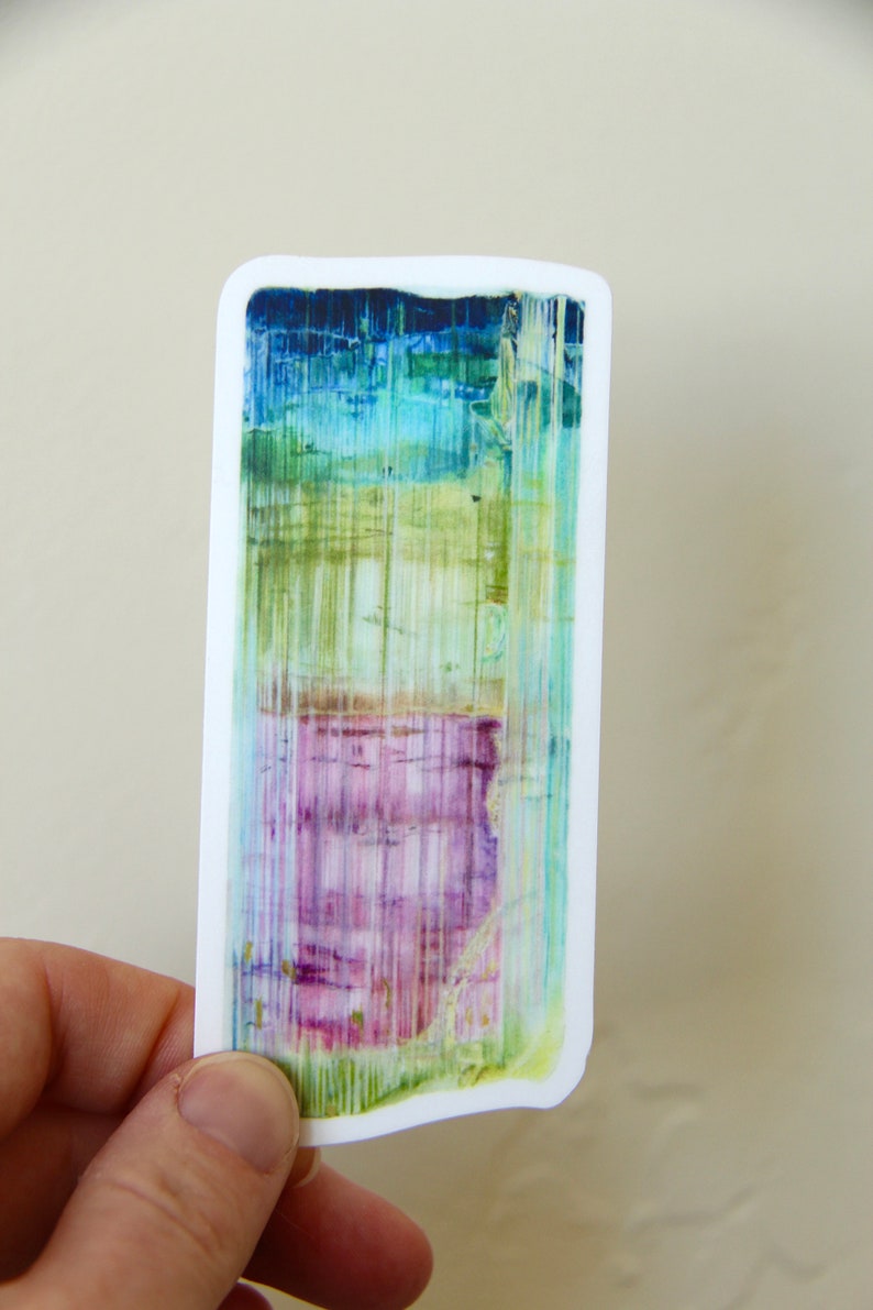 May include: A sticker featuring a colorful abstract design with shades of blue, green, pink, and white. The design resembles a crystal or gemstone with vertical lines.