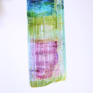 May include: A watercolor painting of a tourmaline crystal. The crystal is a long, rectangular shape with a variety of colors, including green, blue, pink, and purple. The crystal is surrounded by a white background with the word "TOURMALINE" printed below it.