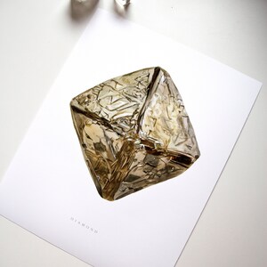 May include: A close-up of a large, clear, faceted diamond with a golden hue. The diamond is on a white background with the word "DIAMOND" printed below it.