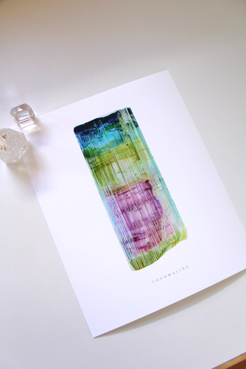 May include: A close-up of a colorful, striated tourmaline crystal. The crystal is a vibrant mix of green, blue, purple, and yellow. The crystal is on a white background with the word "TOURMALINE" printed below it.