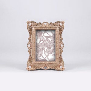 May include: A vintage-style, ornate wooden picture frame with a floral design in the background. The frame is a light brown color with a distressed finish.