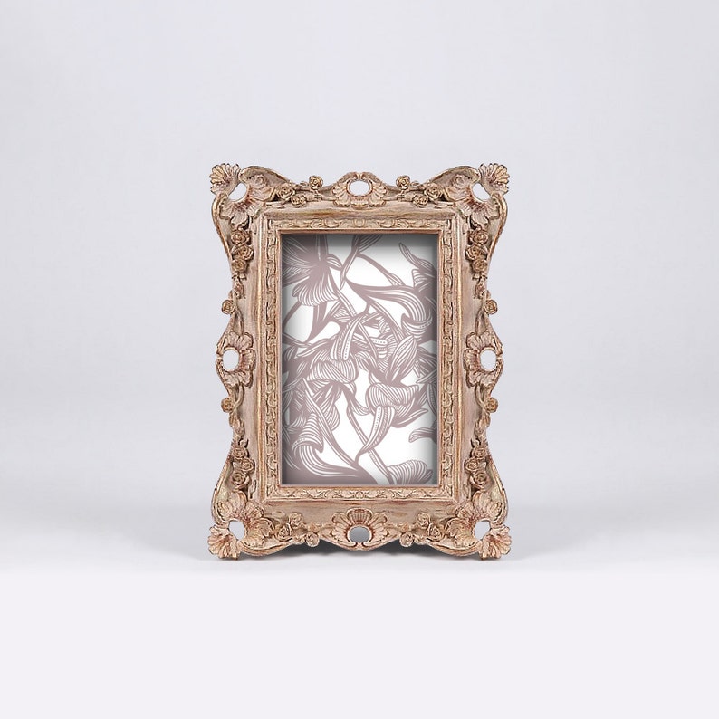 May include: A vintage-style, ornate wooden picture frame with a floral design in the background. The frame is a light brown color with a distressed finish.