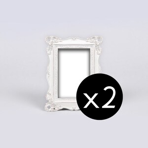 May include: Two white ornate picture frames with a decorative design. The frames are empty and ready to be filled with photos or artwork.