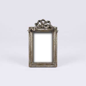 May include: A silver picture frame with an ornate design and a ribbon detail at the top.