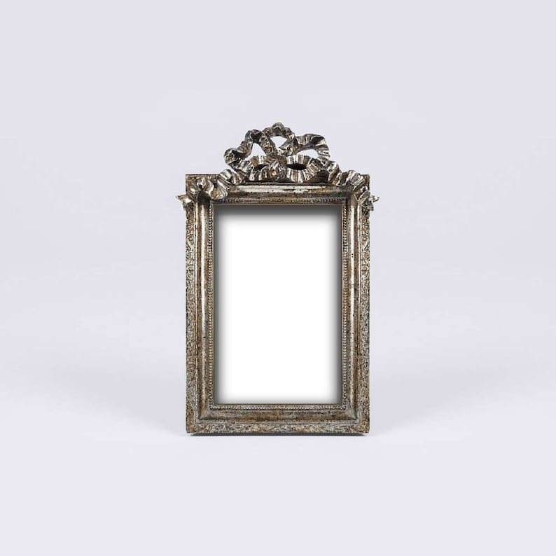 May include: A silver picture frame with an ornate design and a ribbon detail at the top.