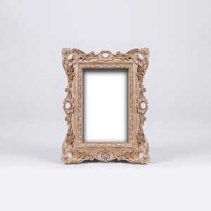 May include: A decorative, ornate picture frame with a light brown finish. The frame has a detailed, carved design with a rectangular opening for a picture.