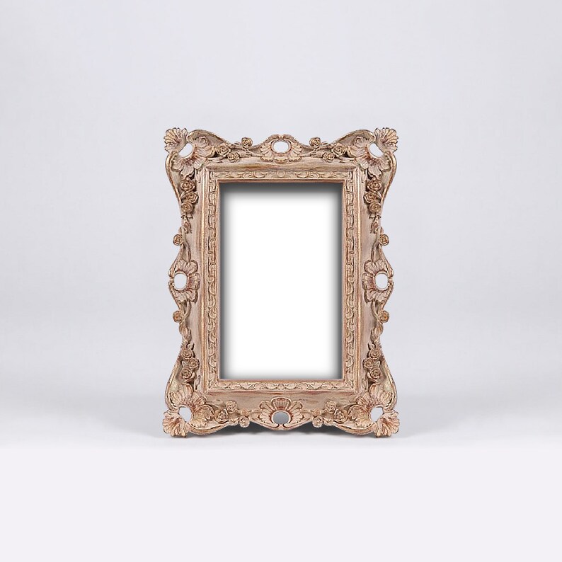 May include: A decorative, ornate picture frame with a light brown finish. The frame has a detailed, carved design with a rectangular opening for a picture.