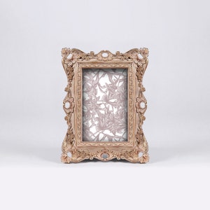 May include: A vintage-style, ornate wooden picture frame with a floral pattern inside. The frame is a light brown color with a distressed finish.