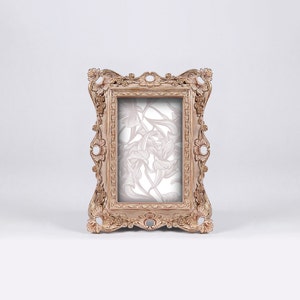 May include: A decorative, ornate, wooden picture frame with a light brown finish. The frame has a floral design inside the glass.