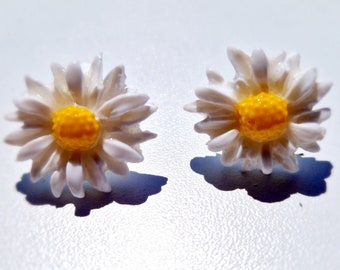 May include: A pair of white daisy earrings with yellow centers. The earrings are small and delicate, perfect for adding a touch of whimsy to any outfit.