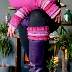 Puede incluir: Un par de polainas de punto a rayas rosa y morado con un calientamanos de punto a rayas rosa y morado sobre una bota morada.