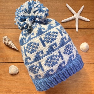 May include: A blue and white knitted hat with a white pom pom on top. The hat has a geometric pattern.
