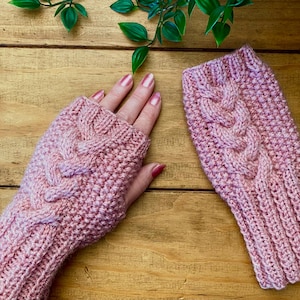 Op de afbeelding: Een paar roze gebreide vingerloze handschoenen met een kabelbreipatroon. De handschoenen zijn gemaakt van zacht garen en hebben een warm, knus gevoel.