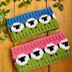 Könnte beinhalten: Zwei gestrickte Stirnbänder mit einem Schaf-Muster. Ein Stirnband ist blau, grün und weiß mit schwarzen Schafen. Das andere Stirnband ist rosa, grün und weiß mit schwarzen Schafen.