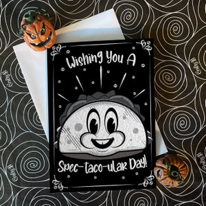 May include: A black and white greeting card with a cartoon taco with eyes and a smile. The card says "Wishing You A Spec-taco-ular Day!"