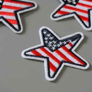 Könnte beinhalten: Drei sternförmige Patches mit einem gestickten amerikanischen Flaggenmuster in Rot, Weiß und Blau.