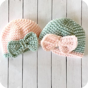 Peut inclure: Deux bonnets pour b&eacute;b&eacute; en crochet avec des n&oelig;uds. Un bonnet est rose avec un n&oelig;ud vert, et l'autre est vert avec un n&oelig;ud rose.