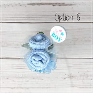 May include: A blue sock flower bouquet with a white and blue "It's a Boy" button. The bouquet is decorated with blue tulle and green leaves.