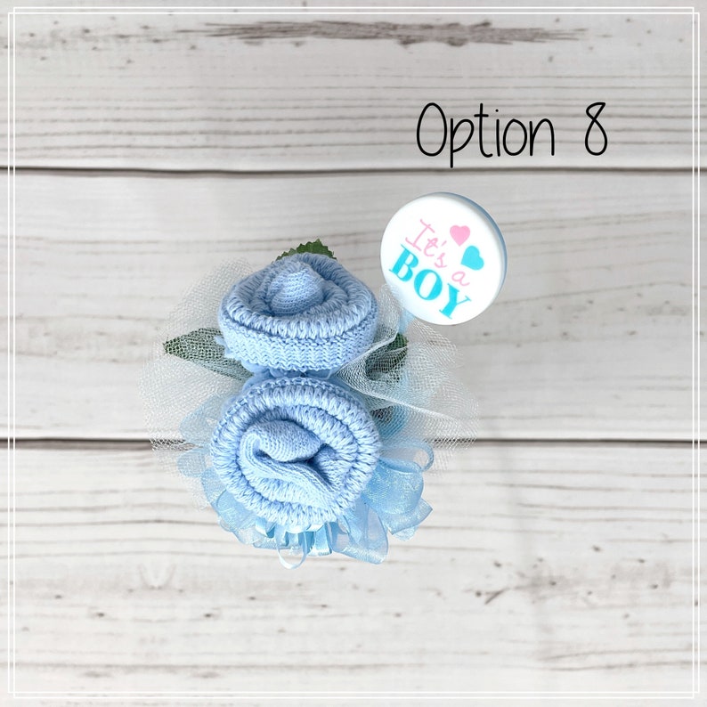 May include: A blue sock flower bouquet with a white and blue "It's a Boy" button. The bouquet is decorated with blue tulle and green leaves.