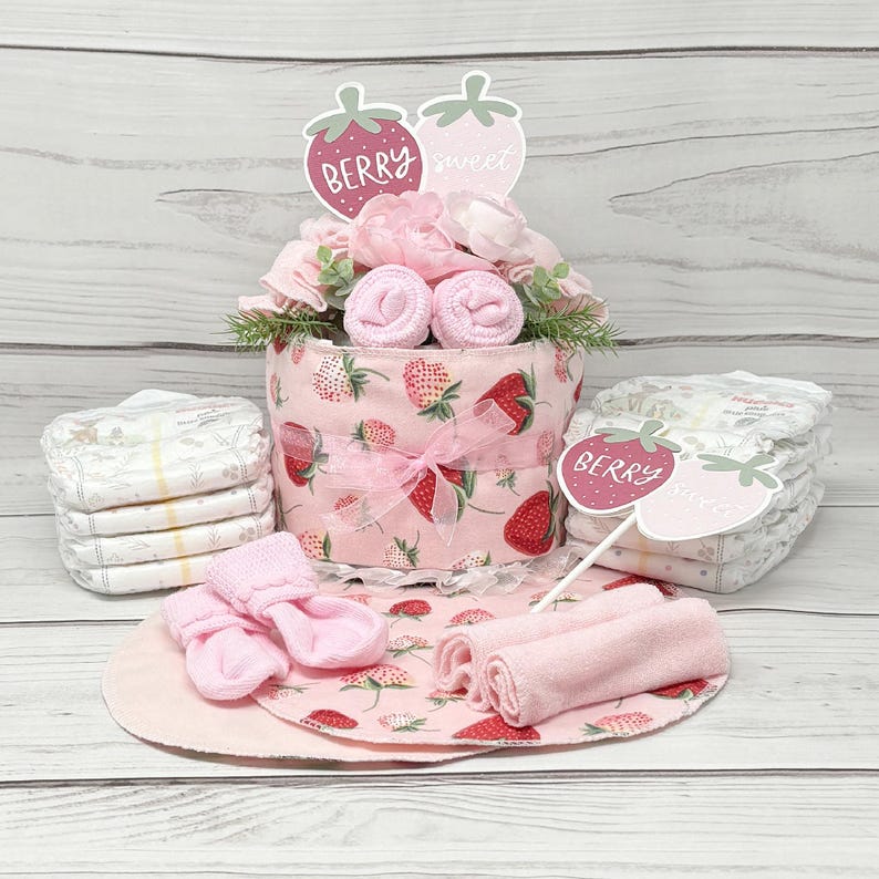 May include: A pink and white diaper cake decorated with strawberries and the words "Berry Sweet" and "Berry". The cake includes pink baby socks, washcloths, and a stack of diapers.