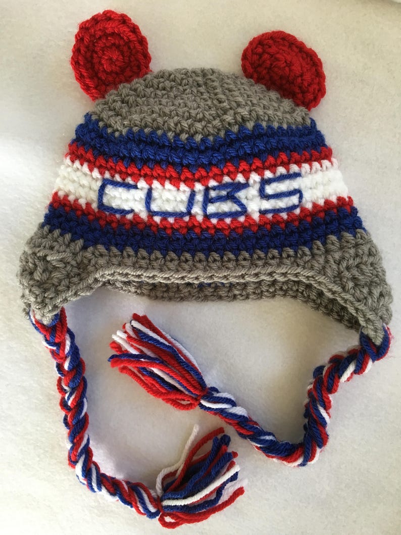 May include: Gray, blue, red, and white crocheted hat with ear flaps and a braided tassel. The hat has the word "CUBS" embroidered on the front.