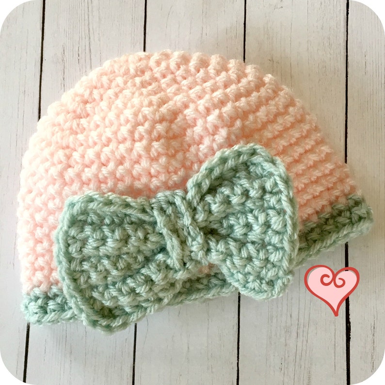 May include: A pink crocheted hat with a green crocheted bow. The hat is made with a single crochet stitch and the bow is made with a double crochet stitch.